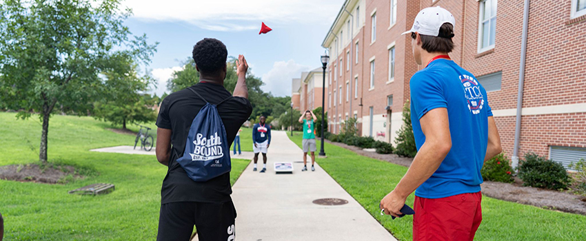 Students playing cornhole outside campus housing.