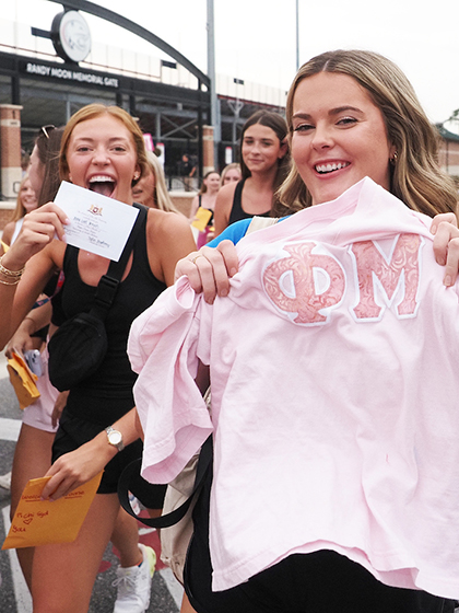 Sorority members holding up sorority shirt and bid day announcement.